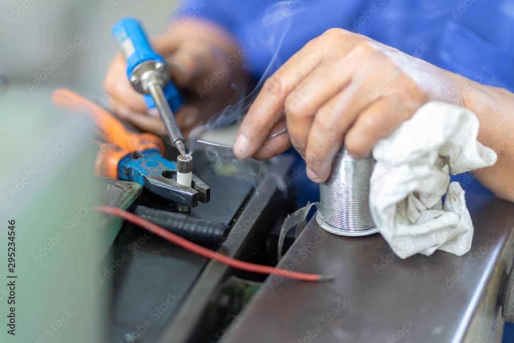 Soldering iron soldering a wire to an electrical component with smoke coming of it lying on top of coloured wires Soldering iron soldering a wire to an electrical component with smoke coming of it lying on top of coloured wires