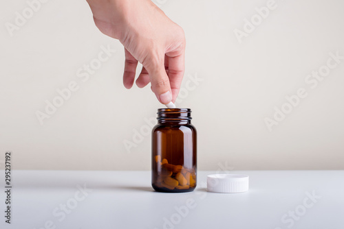 The hand that is picking the supplement out of the bottle on a white background.Dietary supplement product.