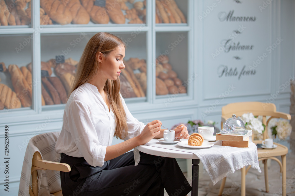 Woman is heaving breakfast with croissant and coffee in the morning. Very beautiful girl with long blonde hair having lunch in a bakery Woman is heaving breakfast with croissant and coffee in the morning. Very beautiful girl with long blonde hair having lunch in a bakery