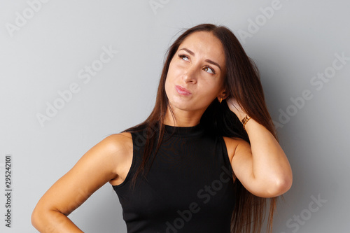 Image of thinking young woman standing over a gray background.