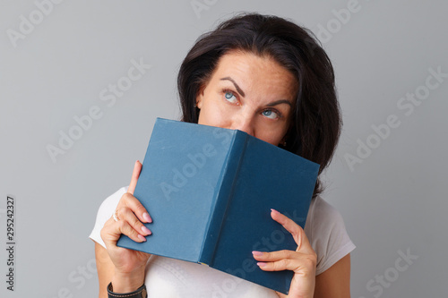 Brunette woman holding a book in her hands over a grey background