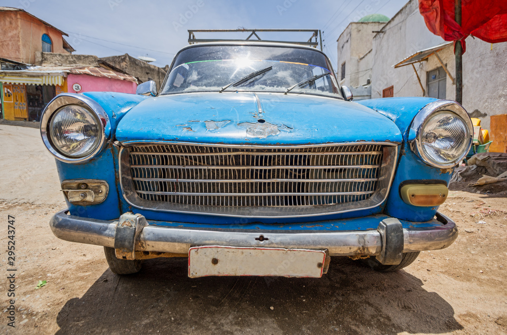 Front part side of an old blue 60's car very used on a dirt road.