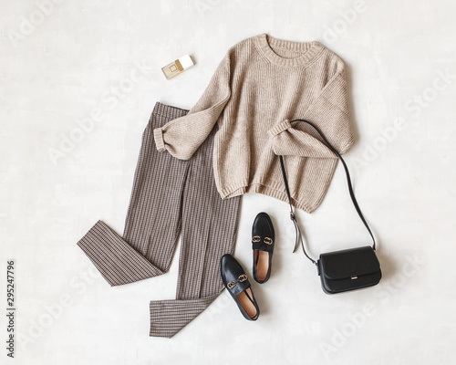 Brown pants in check, beige knitted oversize sweater, cross body bag, black loafers or flat shoes on grey background. Overhead view of women's casual day outfit. Flat lay, top view. Women clothes. photo