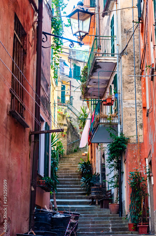 Curved elevated stairs street full of outdoor elements like street lanterns, growing plants, balconies and windows telling their stories about the city life in Monterosso Al Mare, Cinque Terre