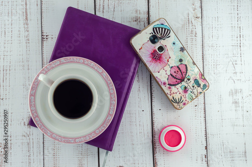 Cup of coffee on a notebook, smartphone, blush on a wooden background