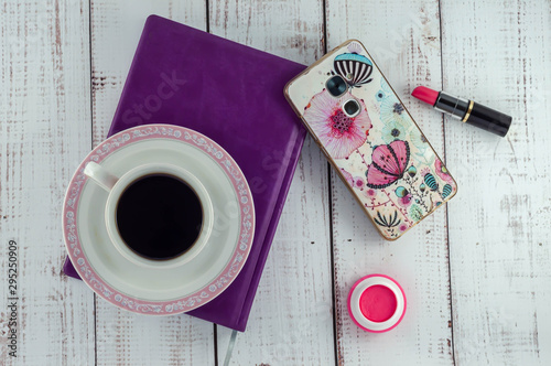 Cup of coffee on a notebook, smartphone, lipstick, blush on a wooden background