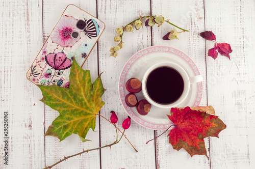 Cup of coffee on a wooden background with autumn maple leaves and chestnuts