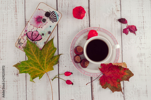 Cup of coffee on a wooden background with autumn maple leaves and chestnuts