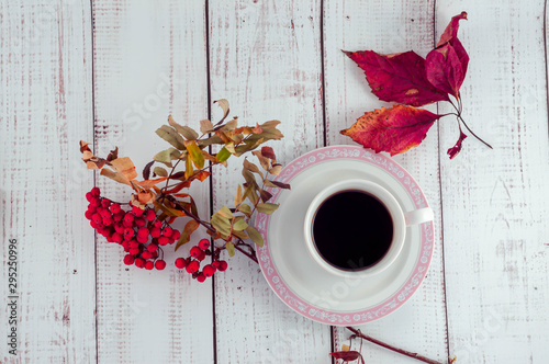 Cup of coffee on a wooden background with autumn leaves and rowan