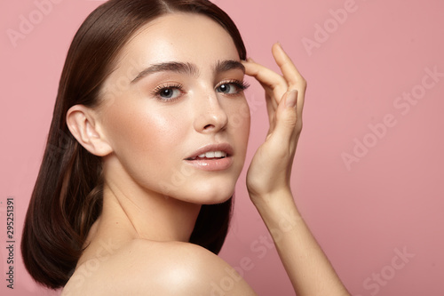 young girl with hand near face with clean skin, natural makeup and white teeth on a pink background
