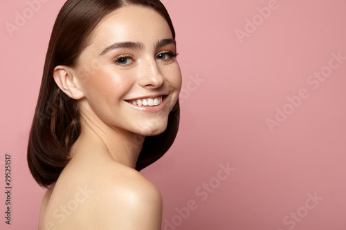 Beautiful smiling woman with clean skin, natural makeup and white teeth on a pink background