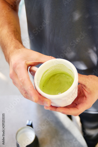 Male barista making vegan matcha cappuccino with oat milk