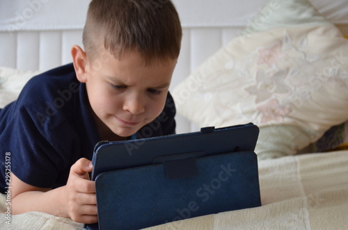 little boy at expressive face using a digital tablet in bed plays games, watch cartoons, talks with friends, writes a message