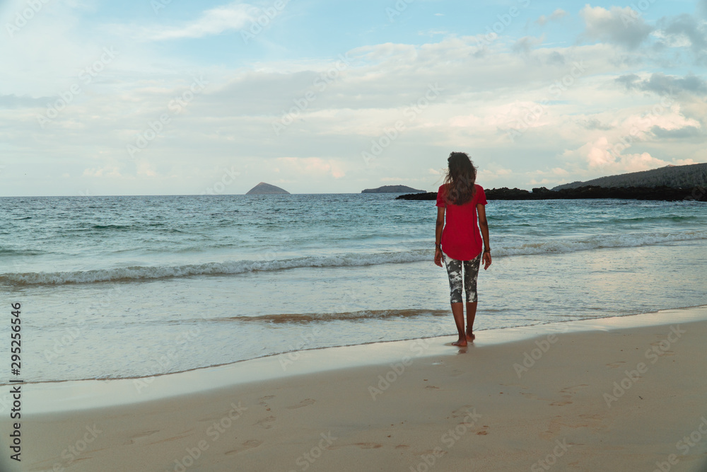 Woman walking on sandy beach. Tropical travel concept. Holiday, vacation vibes, with turquoise ocean waves and white sand. Love, romance, happy. Shot in San Cristobal, Galapagos Islands.