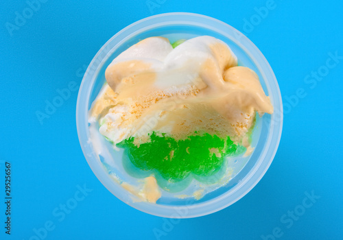 top view cup of orange and green color ice cream with some bites on blue background