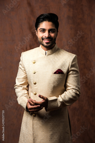 Indian bridegroom wears ethnic or traditional kurta / cloths.  Male fashion model in sherwani, posing / standing against brown grunge background, selective focus