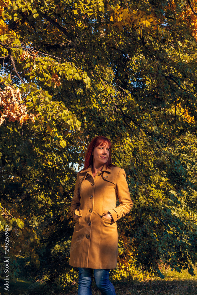 Colorful foliage in the park. Falling leaves natural background. Red hair woman in nature.