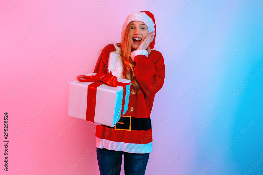 Happy excited woman in Santa hat with gift box on background with neon light Happy excited woman in Santa hat with gift box on background with neon light