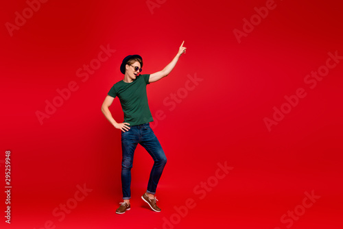 Full size profile side photo of crazy guy have fun on summer weekends celebration aprty dance raise index finger wear denim jeans sneakers outfit isolated over red color background