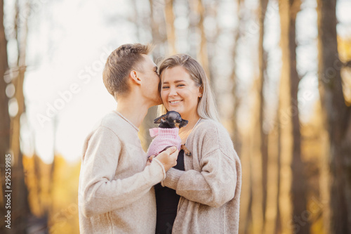 Loving couple cuddles in warm bright sweaters holding dwarf dog in their hands.Concept Childfree photo
