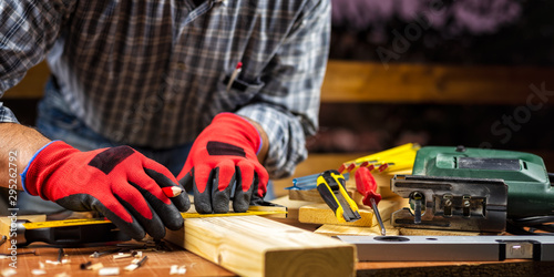 Adult carpenter craftsman wears protective gloves, with a pencil and the carpenter's square trace the cutting line on a wooden table. Construction industry, housework do it yourself. Stock photography