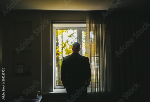 Silhouette of man in suit standing near big window and looking on autumn nature. Rear view.