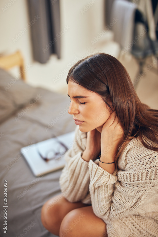 Attractive caucasian brunette having neck pain. Bedroom interior. Attractive caucasian brunette having neck pain. Bedroom interior.