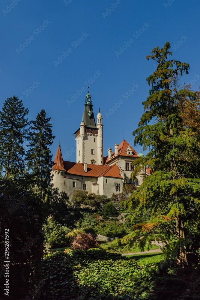 Pruhonice, Czech Republic - October 7 2019: Scenic view of famous romantic castle standing on a hill surrounded with tall green trees. Sunny autumn day with blue sky. Vertical image.