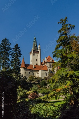 Pruhonice, Czech Republic - October 7 2019: Scenic view of famous romantic castle standing on a hill surrounded with tall green trees. Sunny autumn day with blue sky. Vertical image.
