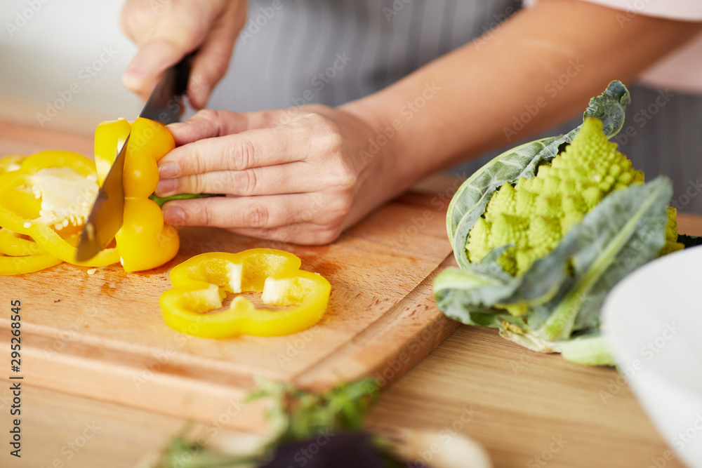 Close-up of woman cutting yellow fresh pepper with knife on cutting board she preparing dinner