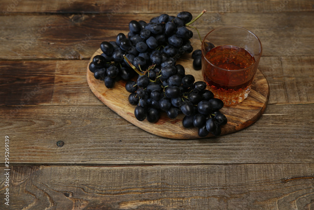 glass of brandy or wine and a juicy bunch of black grapes on a wooden rustic table. With copy space for text. glass of brandy or wine and a juicy bunch of black grapes on a wooden rustic table. With copy space for text.