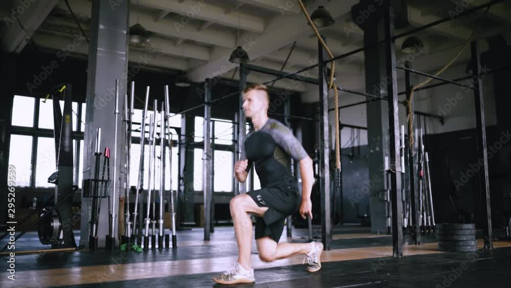 Static view, hardy and enduring man do exercise and train in gym. Modern gym for crossfit and yoga. Muscle guy do forward lunges with squat. Exercises fo running Static view, hardy and enduring man do exercise and train in gym. Modern gym for crossfit and yoga. Muscle guy do forward lunges with squat. Exercises fo running