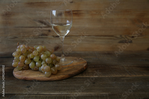 glass of white wine and bunch of grapes on a wooden table. With copy space for text.