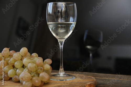 glass of white wine and bunch of grapes with reflection in glass on a wooden table