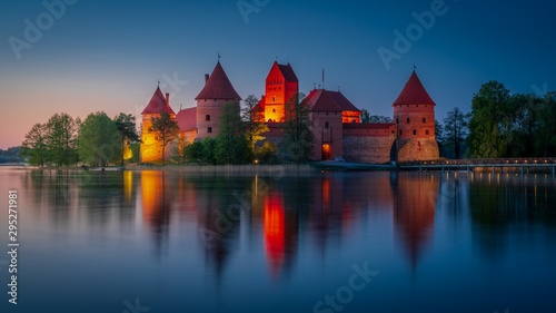 Beautiful medieval castle with red roofs and brick walls reflecting in calm lake at night. Travel destinations