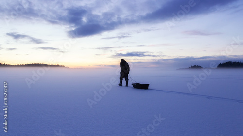 Man silhouette walk on the ice surface covored by snow at evening. Frozen Lake and forest silhouette. Hiking concept.