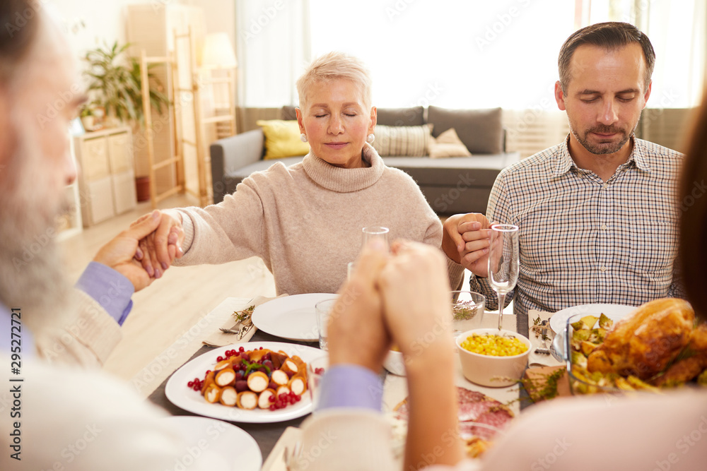 Εκτύπωση καμβά Beautiful couple with eyes closed sitting at dining table holding hands and pray