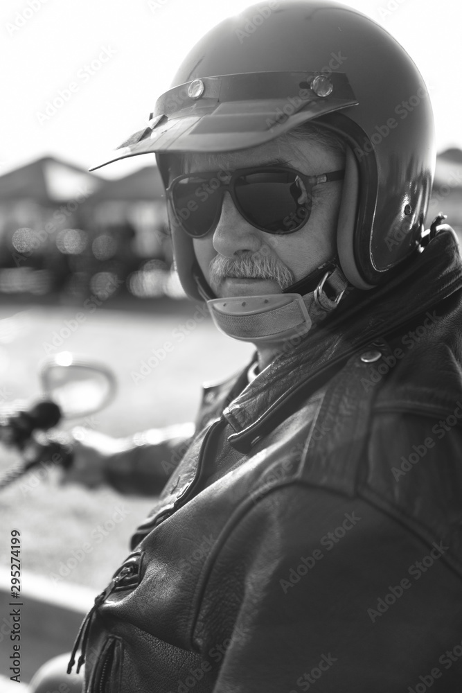 black and white portrait of a middle-aged man, an old biker in a leather jacket on a retro bike, vintage classic motorcycle. concept of freedom and style, a hobby for life. close up vertical photo