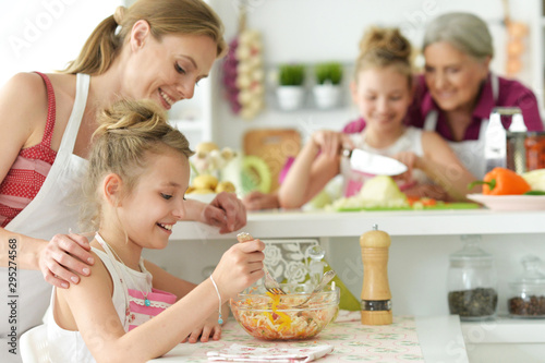 Portrait of cute girls with mother preparing delicious fresh salad in kitchen