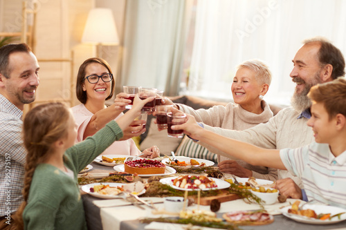 Happy big family sitting at dining table and toasting with red wine together while celebrating holiday at home