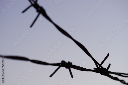 black silhouette of a barbed wire fence closeup in evening blue sky.