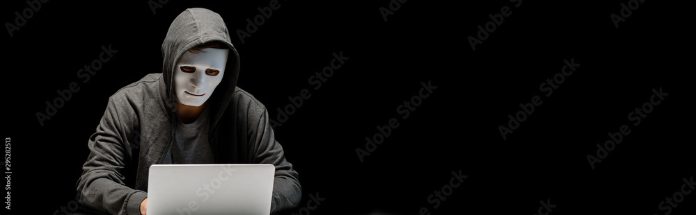 panoramic shot of anonymous internet troll in mask typing on laptop keyboard isolated on black