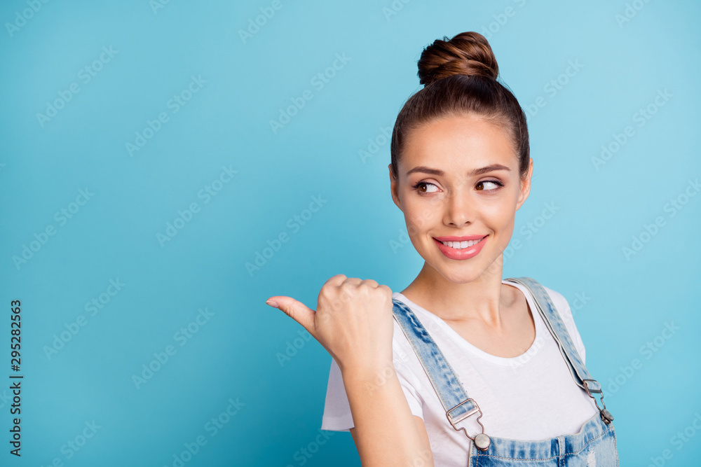Portrait of charming lady showing at copy space by her forefinger looking wearing white t-shirt denim jeans overalls isolated over blue background Portrait of charming lady showing at copy space by her forefinger looking wearing white t-shirt denim jeans overalls isolated over blue background