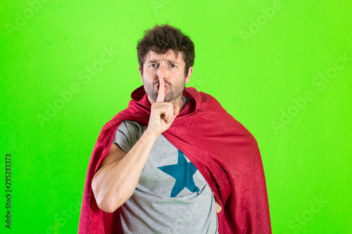 Young crazy superhero making a silence gesture or sign over green background