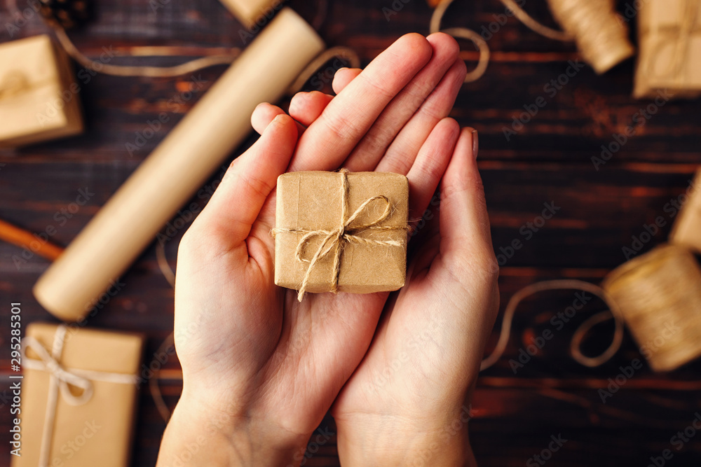 Obraz premium Women's hands hold a gift of craft paper. Against the background of dried orange, cinnamon, pine cones, anise on a wooden table.