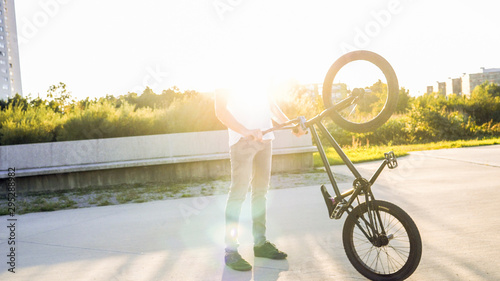 Unrecognizable young BMX rider in park s holding up BMX bicycle on sunny summer day