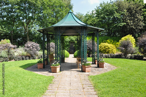 Large  hexagonal gazebo provides shade for seating inEnglish formal garden 