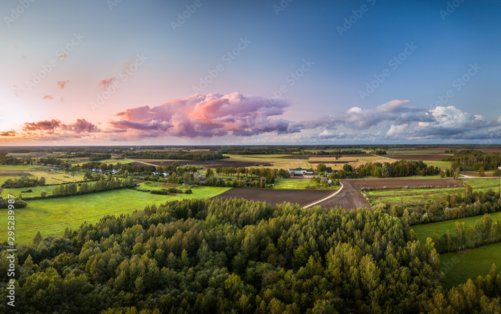 Naklejka premium Aerial view on impressive storm clouds over forest in colorful sunset colors. Dark storm clouds covering the rural landscape. Intense rain shower in distance.
