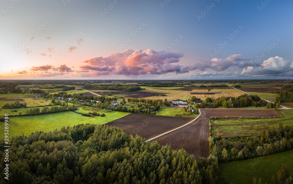 Aerial view on impressive storm clouds over forest in colorful sunset colors. Dark storm clouds covering the rural landscape. Intense rain shower in distance. 
