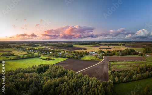Aerial view on impressive storm clouds over forest in colorful sunset colors. Dark storm clouds covering the rural landscape. Intense rain shower in distance. 